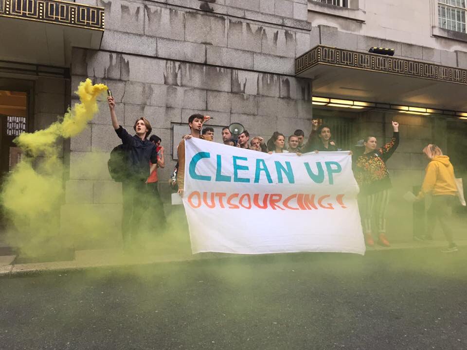 Student activists stand outside Senate House, holding a banner which says 'Clean Up Outsourcing!'